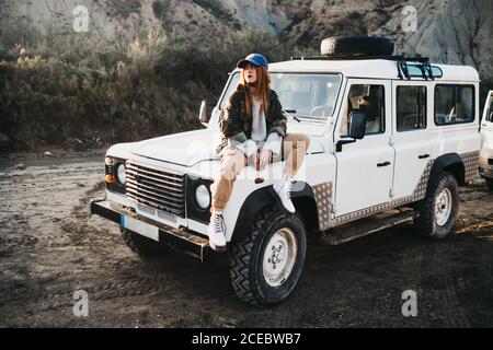 Junge Frau in Freizeitkleidung sitzt auf dem Auto Stockfoto