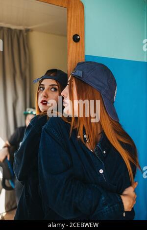 Junge charmante rothaarige Frau in Freizeitkleidung mit gekreuzten Händen Blick auf Reflexion in der Nähe der blauen Wand Stockfoto
