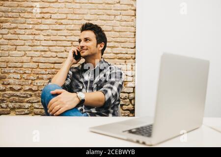 Junger Mann mit Smartphone am Tisch mit Laptop Stockfoto