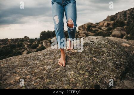 Aufnahme einer Frau in stilvollem Denim, die barfuß auf rauem, grauem Felsbrocken gegen bewölkten Himmel läuft Stockfoto