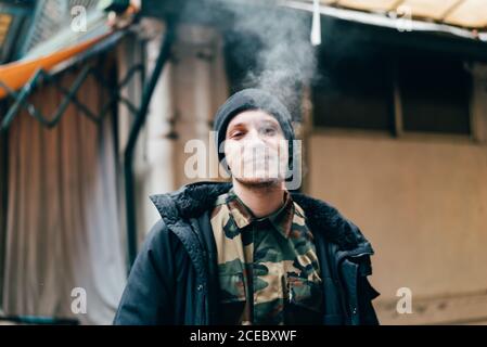 Hübscher junger Mann, der auf der Straße steht und raucht. Stockfoto