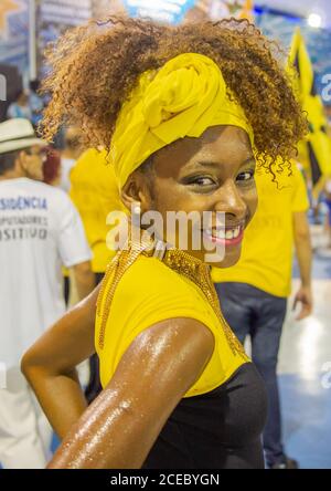 Rio de Janeiro, Brasilien - 13 2014. Februar: Seitenansicht einer schönen ethnischen Frau in hellem Kostüm, fröhlich lächelnd und beim Blick auf die Kamera während der Proben in der Samba-Schule Stockfoto