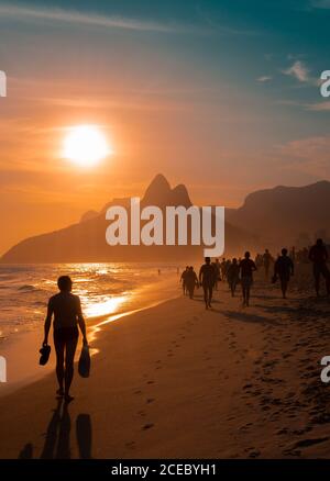 Rio de Janeiro, Brasilien - Februar, 12 2014: Gruppe von anonymen Menschen zu Fuß auf sandigen Ipanema Strand in der Nähe winkende Meer während herrlichem Sonnenuntergang Stockfoto