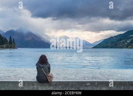 Christchurch, Neuseeland - März, 17 2015: Rückansicht der Frau in lässigem Outfit mit Blick auf ruhigen See und erstaunliche Berge am bewölkten Tag Stockfoto