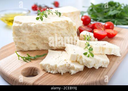 Schmackhafter Schaf- oder Ziegenkäse. Stücke von Adyghe Käse auf einem Holzbrett auf weißem Hintergrund. Landwirtschaftliche Bio-Produkte. Stockfoto