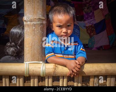 Sulawesi Island, Indonesien - August, 15 2015: Süßer kleiner ethnischer Junge, der an sonnigen Tagen im Dorf auf der Bambusterrasse steht und vor die Kamera schaut Stockfoto