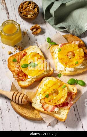 Gesundes Frühstück oder Snack, Snacks. Toast mit karamellisierter Ananas, Speck, Nüssen und Ricotta auf dem Küchentisch. Stockfoto