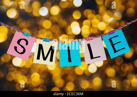 Die Buchstaben LÄCHELN Zeichen hängen auf einer Wäscheklammer auf einem Hintergrund von farbigen Lichtern. Stockfoto