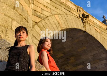 Von unten Schuss von attraktiven asiatischen Frauen, die sich auf alt Backsteinbrücke, während Sie am sonnigen Tag Zeit im Park verbringen Stockfoto