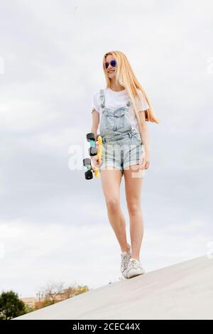 Blonde Mädchen mit Penny Board zu Fuß im Park Stockfoto