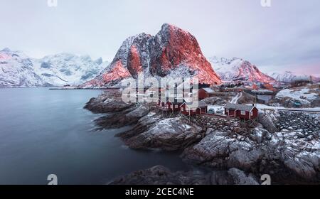 Malerischer Blick auf kleine Dorf rote Häuser an der felsigen Küste von ruhigen Meer Hafen mit Bergen, Lofoten Insel Stockfoto
