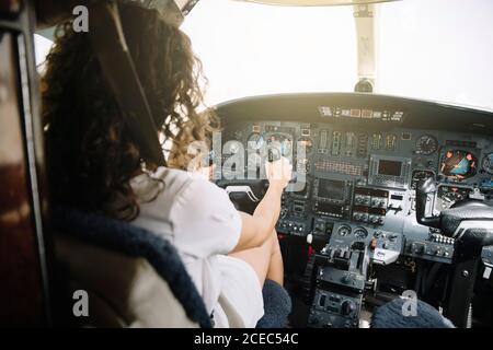 Rückansicht einer brünette Frau mit lockigen Haaren, die im Cockpit sitzt und im Flugzeug navigiert Stockfoto