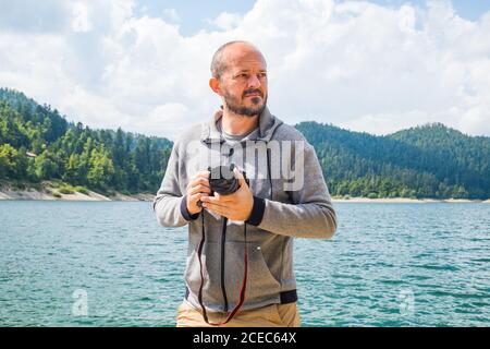 Fotograf Mann im Hoodie Wandern rund um See mit DSLR-Kamera und schießen Natur, Halb-Body-Portrait, Landschaftsfotografie Konzept Stockfoto