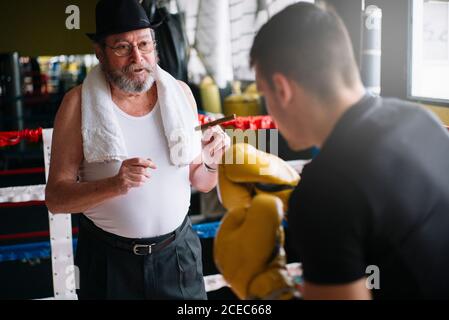 Seitenansicht des Boxermanns, der die Handschuhe des Trainers in der Turnhalle stanzt. Stockfoto