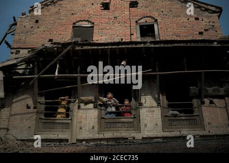 Kinder spielen an den Fenstern eines Hauses, das durch die Erdbeben in Nepal 2015 in Bhaktapur, Bagmati Pradesh, Nepal, stark beschädigt wurde. Stockfoto