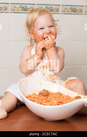 Fröhliches kleines Kind auf Geschichte sitzen und Spaß beim Essen Pasta aus Schüssel. Stockfoto