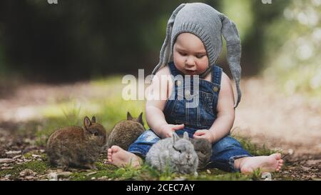 Niedliches kleines Kind in grauem Hut sitzt mit Hasen im Park. Stockfoto