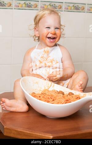 Fröhliches kleines Kind auf Geschichte sitzen und Spaß beim Essen Pasta aus Schüssel. Stockfoto