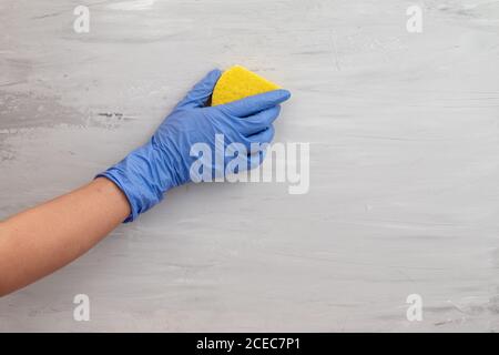 Hand in einem Handschuh hält einen gelben Schwamm und wäscht eine Wand. Leerer Platz für Text Stockfoto