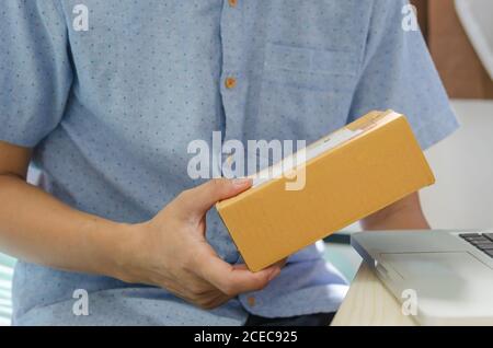 Die Hände des Mannes halten das Paket und den Laptop am Tisch. Stockfoto