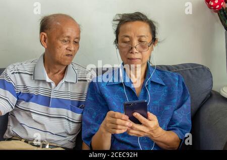 Porträt eines älteren asiatischen Paares mit einem Mobiltelefon Um Musik zu hören Stockfoto