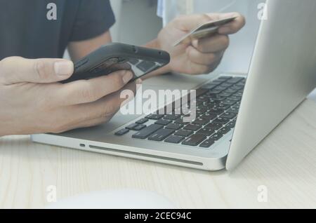 Mann Einkaufen Online mit Laptop mit Kreditkarte.Hände halten Kreditkarte und Smartphone. Stockfoto