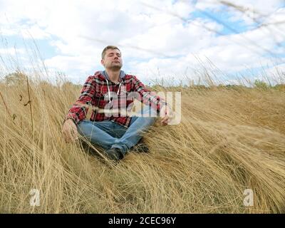 Der junge Tourist sitzt im Gras auf dem Herbstfeld. Entspannung und Meditation. Stockfoto