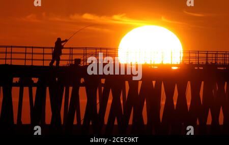 Ein Mann, der im frühen Morgenlicht fischt, während die Sonne über Blyth Pier in Northumberland am ersten Tag des Meteorologischen Herbstes aufgeht. Stockfoto