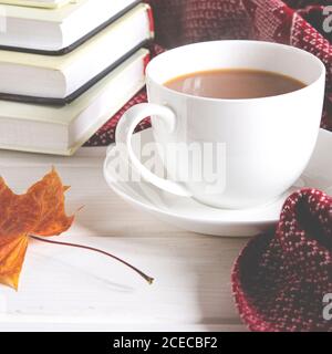 Eine Tasse Kaffee mit Milch steht auf dem Tisch neben Büchern und eine warme Wolle Schal Stockfoto