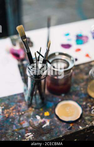 Die Pinsel im Glasgefäß auf dem Tisch in den Farbflecken angeordnet. Stockfoto