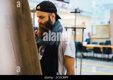 Bärtiger Mann, der auf Staffelei zeichnet Stockfoto