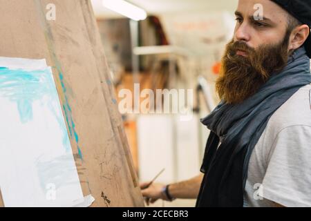 Bärtiger Mann, der auf Staffelei zeichnet Stockfoto