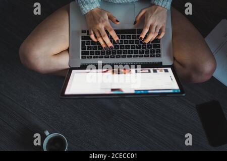 Von oben nicht erkennbare Frau mit Laptop auf dem Boden sitzen und tippen. Stockfoto
