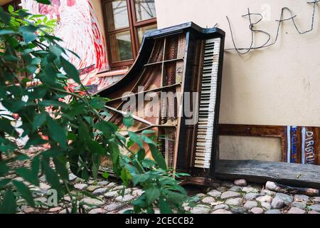 Altes kaputtes Klavier, das in der Nähe des Gebäudes auf einem Steinpflaster lag Kleine Stadtstraße Stockfoto