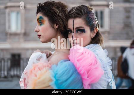 Seitenansicht von zwei jungen Frauen mit Theater Make-up und Ungewöhnliche Kleidung Durchführung und Umarmung auf der Straße der Stadt Stockfoto