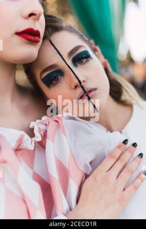 Schöne junge Frau mit theatralischen Make-up umarmen Freund und Blick auf die Kamera, während in der Nähe von fröhlichen Go-round auf dem Messegelände stehen Stockfoto