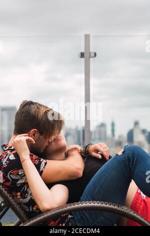 Seitenansicht von niedlichen jungen Paar Augen geschlossen halten Und kuscheln, während Sie auf einer bequemen Liege auf der Terrasse liegen Moderne Stadt Stockfoto