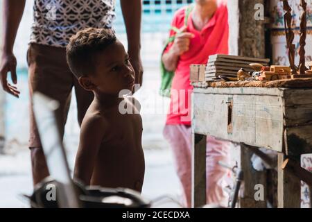 LA HABANA, KUBA - 6. NOVEMBER , 2018: Seitenansicht eines kleinen nachdenklichen hispanischen Jungen, der Holzfiguren in der Nähe von Kulturpflanzen in Kuba betrachtet Stockfoto