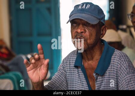 LA HABANA, KUBA - 6. NOVEMBER , 2018: Afroamerikanischer Mann im Alter in Mütze und Polo im Raum zwischen den Menschen in Kuba auf verschwommenem Hintergrund sprechen Stockfoto
