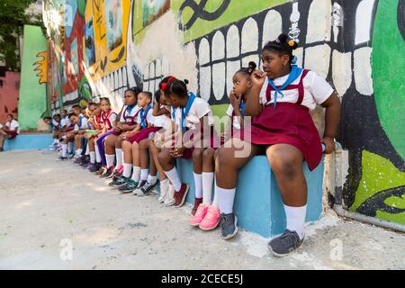 LA HABANA, KUBA - 6. NOVEMBER 2018: Afroamerikanische fröhliche Jugendliche in Pionieruniform sitzen in Kuba neben bemalten Wänden und vorbeiziehenden Steinen Stockfoto