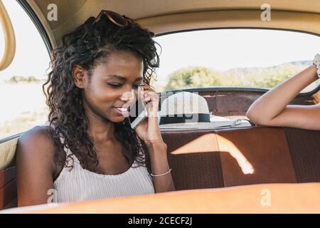 Junge afroamerikanische Frau, die mit Reisenden Freunden auf dem Rücksitz eines alten Autos telefoniert Stockfoto