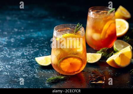 Eistee mit Zitrone, Limette und Eis garniert mit Rosmarin. Gefrorene Gläser mit Zitrusscheiben auf einem dunkelblauen Tisch. Speicherplatz kopieren. Stockfoto