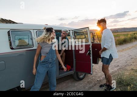 Junge Männer und Frauen steigen aus einem Retro-Van aus, während sie gemeinsam in der wunderschönen Natur unterwegs sind Stockfoto