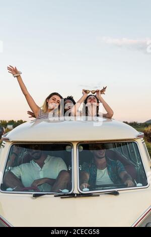 Gruppe von verschiedenen jungen Freunden, die in Luke im Dach stehen Von Oldtimer und Blick auf die Kamera während der Zeit In der Natur zusammen Stockfoto