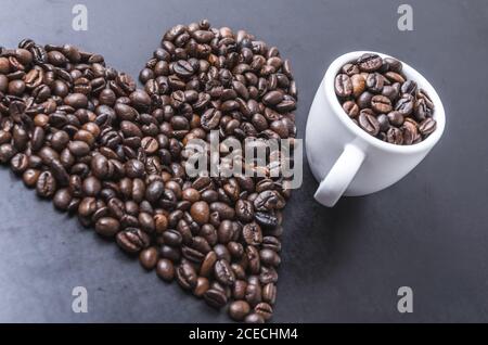 Kaffeebohnen mit Tasse auf dunklem Hintergrund, herzförmig, Nahaufnahme Stillleben, flach legen, innen Studio, Ich liebe Kaffee-Konzept Stockfoto