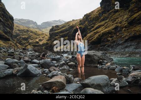 Junge schöne weibliche stehend im Badeanzug in Mountain River Mit großen Steinen mit Händen nach oben Stockfoto