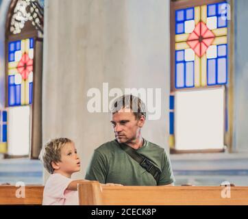 Christian Papa erzählt seinem Sohn biblische Geschichten über Jesus in kirk sitzen. Glaube, Religionsunterricht, moderne Kirche, Vatertag, väterliche Stockfoto