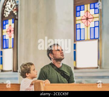 Christian Papa erzählt seinem Sohn biblische Geschichten über Jesus in kirk sitzen. Glaube, Religionsunterricht, moderne Kirche, Vatertag, väterliche Stockfoto