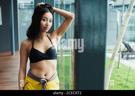 Junge hübsche asiatische Frau in Sportkleidung, die Haare hält und die Kamera anschaut. Stockfoto