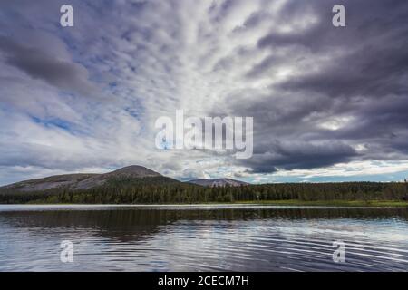 Landschaft von schönen hohen Bergen hinter grünen Wald in der Nähe Klarer plätschernder See vor dem Hintergrund des wolkigen Himmels Stockfoto